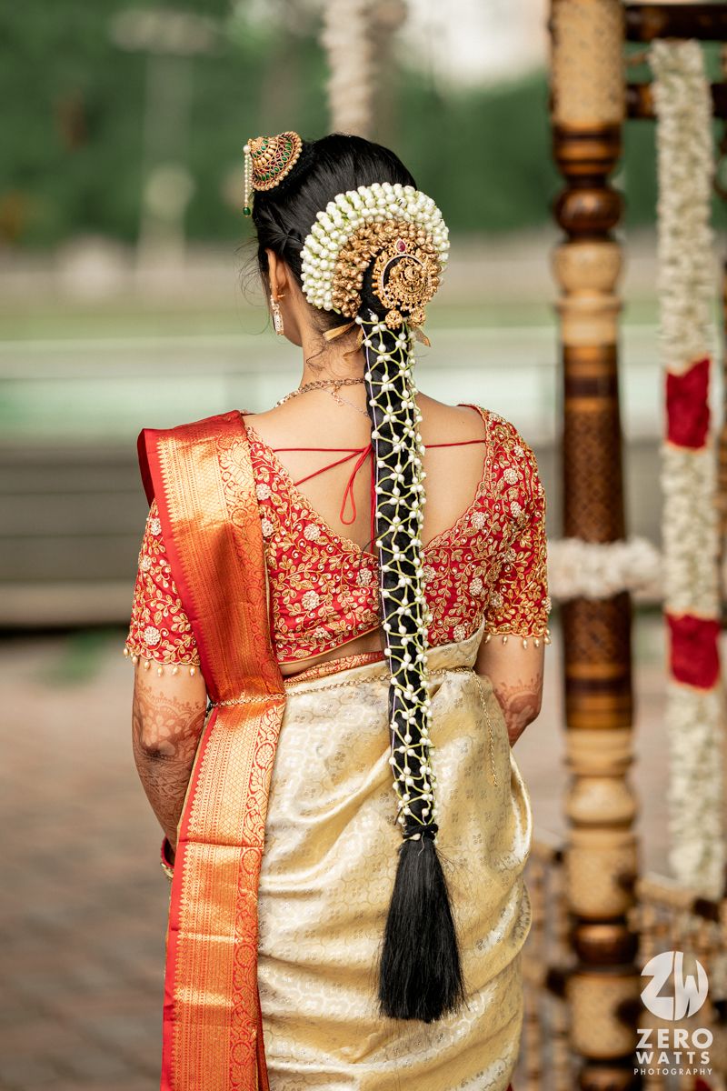 Close-up of traditional South Indian bridal attire showing a gold silk saree with red border and jasmine flower hair decoration.