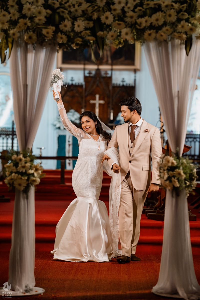 Newlyweds celebrating under a floral arch with white drapes in a church ceremony.