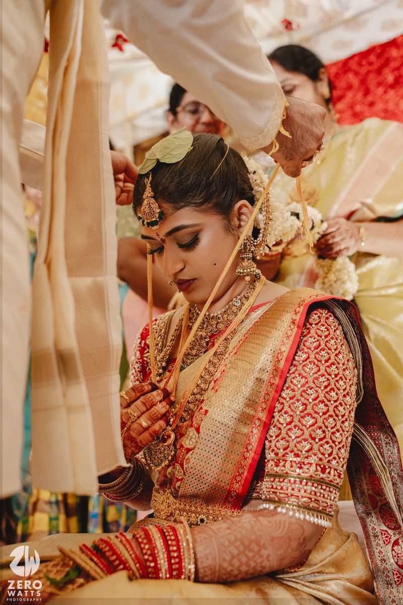 Traditional Indian bride wearing ornate red and gold embroidered lehenga with intricate jewelry at wedding ceremony.