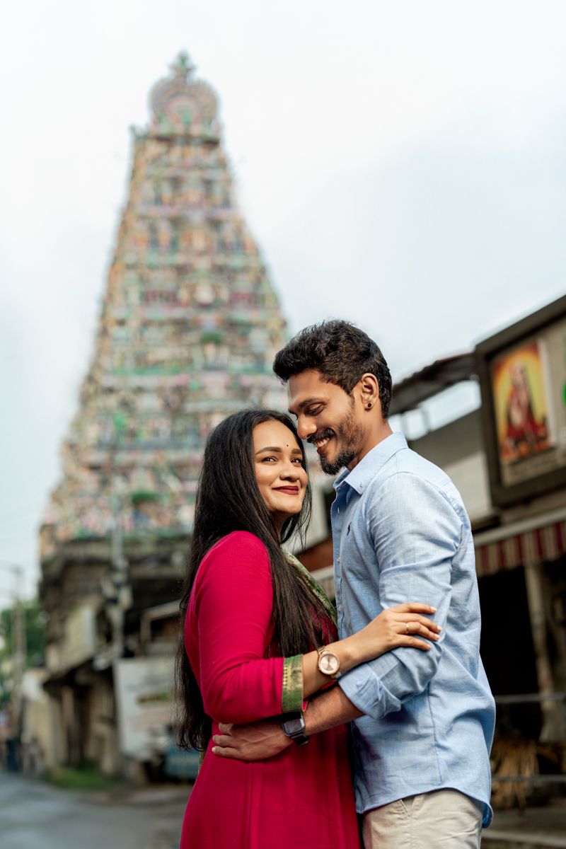 A couple embraces lovingly in front of an ornate Hindu temple with traditional South Indian architecture.