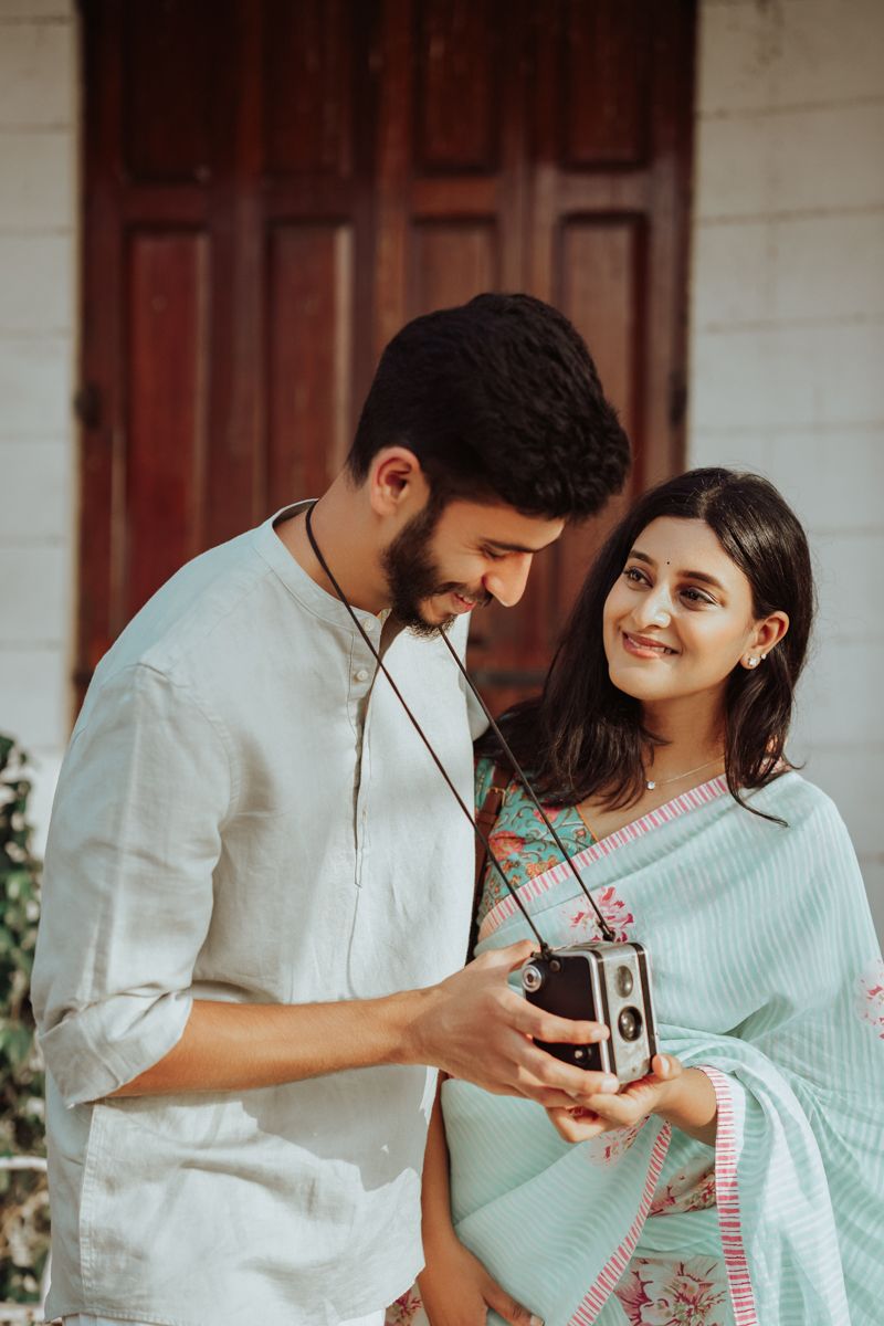 Couple sharing a vintage camera moment together while wearing traditional Indian attire in soft natural lighting.