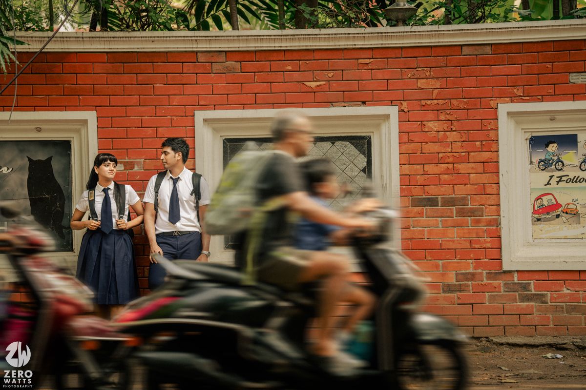 Motion blur of cyclists passing by red brick building with windows on sunny day.