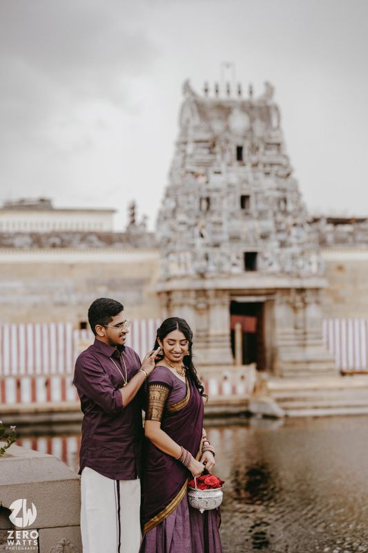 Romantic couple shares candid moments at a historic temple site with traditional white and purple outfits.