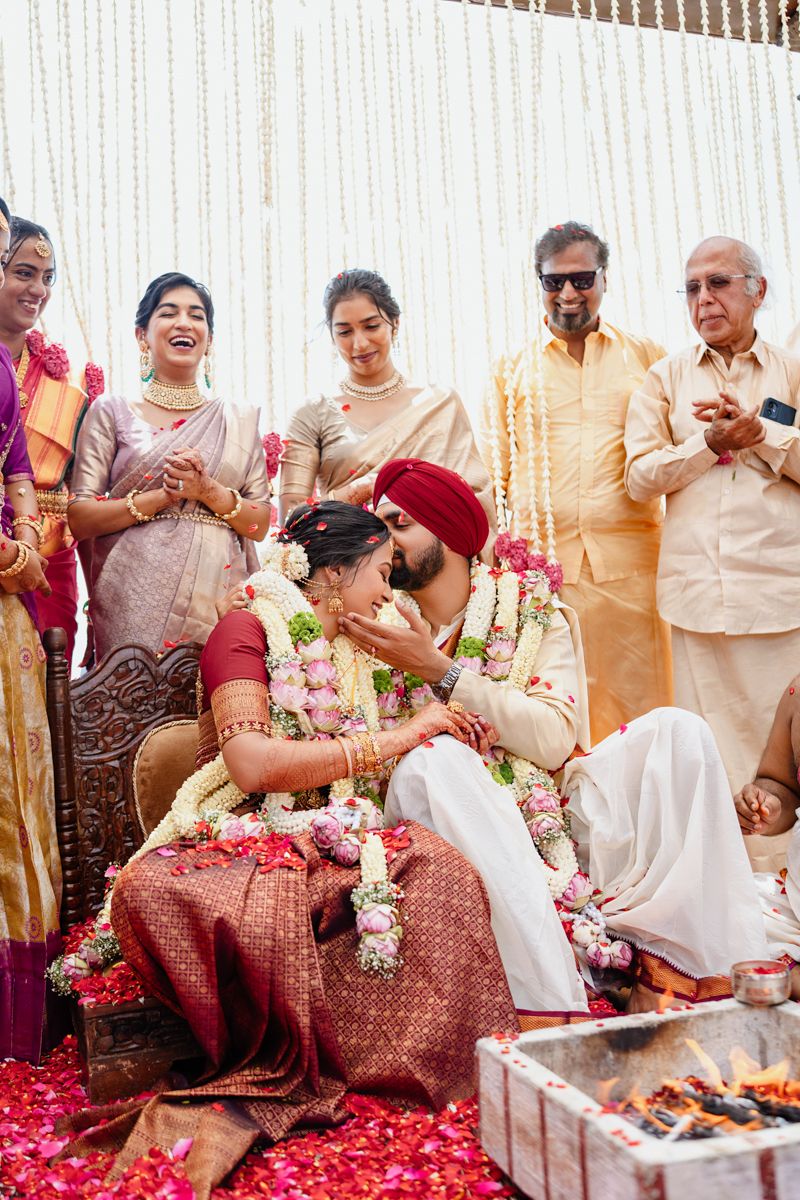 Traditional Indian wedding ceremony with guests seated on floor amid pink flower petals and decorations.