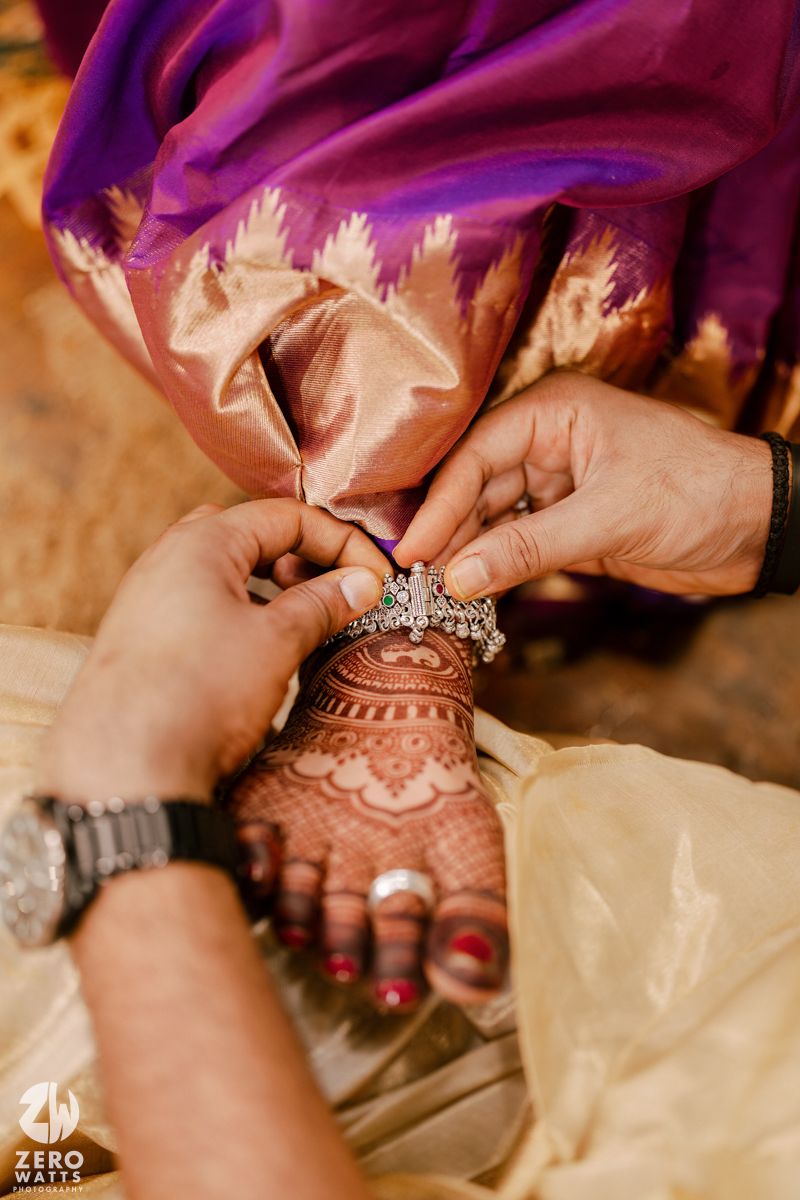 Close-up of hands adorned with henna applying jewelry during wedding ceremony.