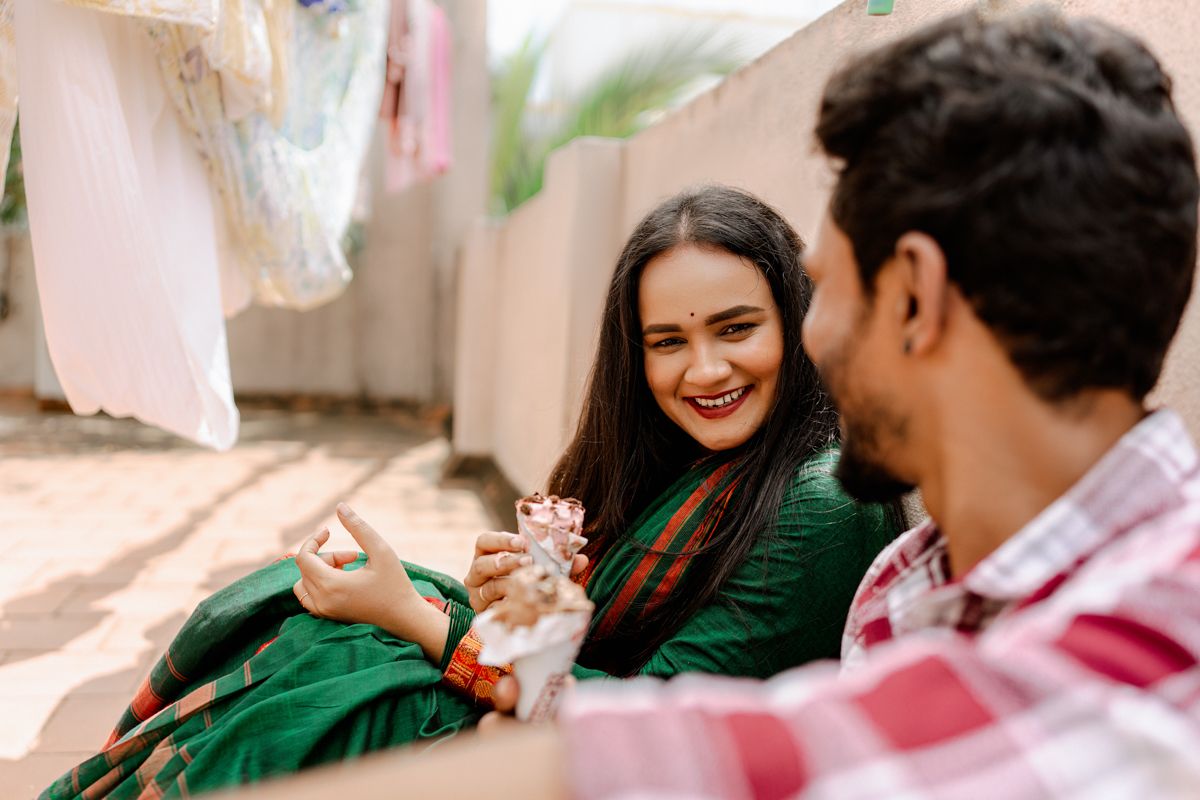 A couple shares a joyful moment together while sitting outdoors, with one wearing a green dress and the other in a plaid shirt.