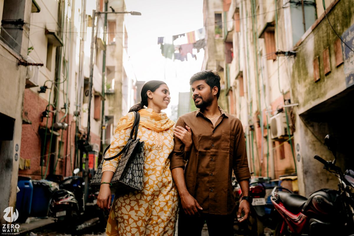 A couple shares a romantic moment while walking through narrow alleyways lined with old buildings in an urban setting.