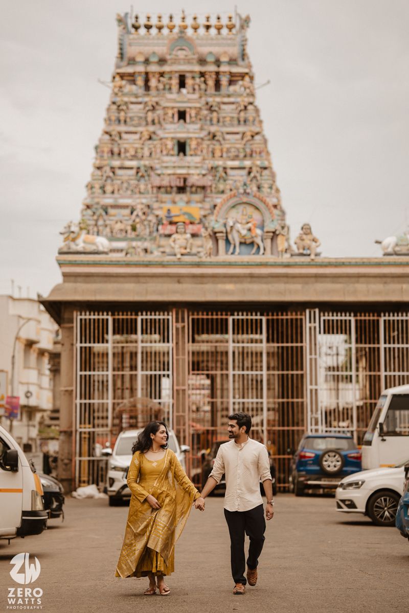 Couple walks hand in hand in front of an ornate temple with traditional South Indian Dravidian architecture.