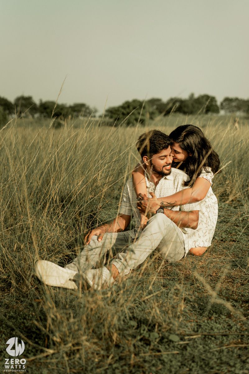 A couple embraces while sitting in tall grass during golden hour.