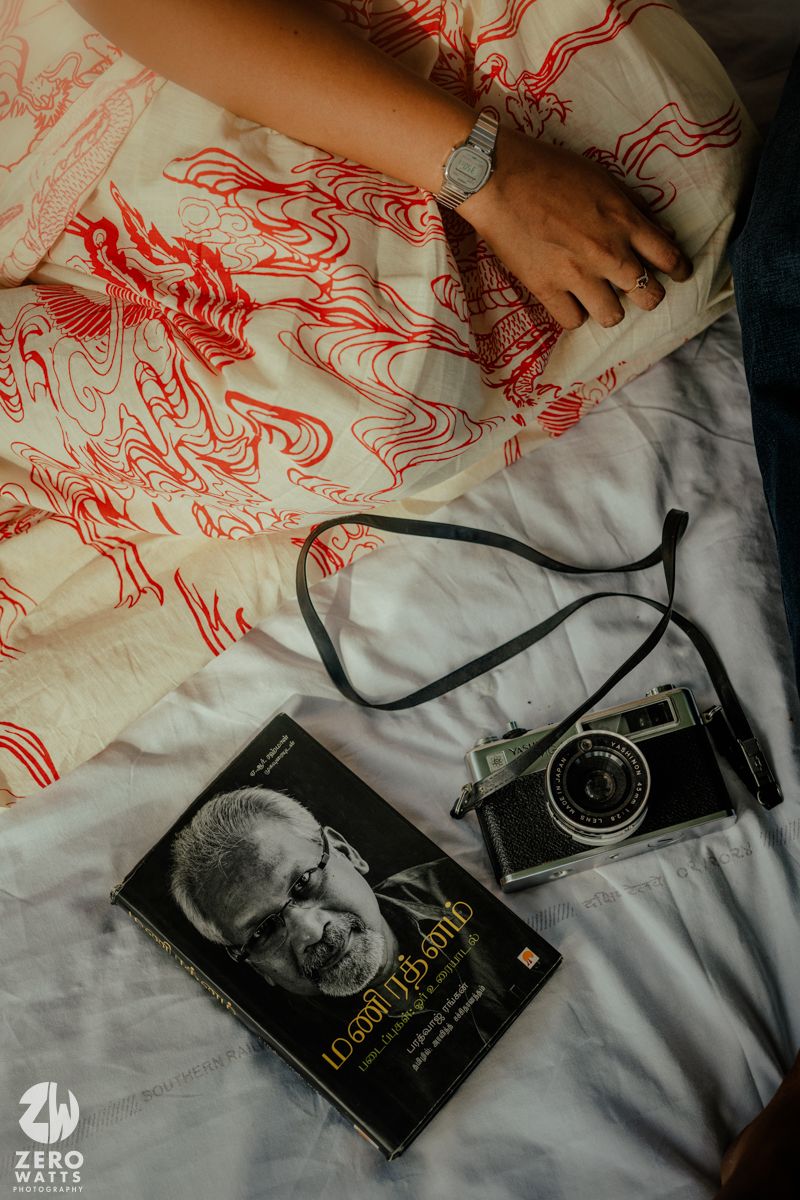 A white fabric with red dragon patterns lies next to books and camera equipment on a bed.