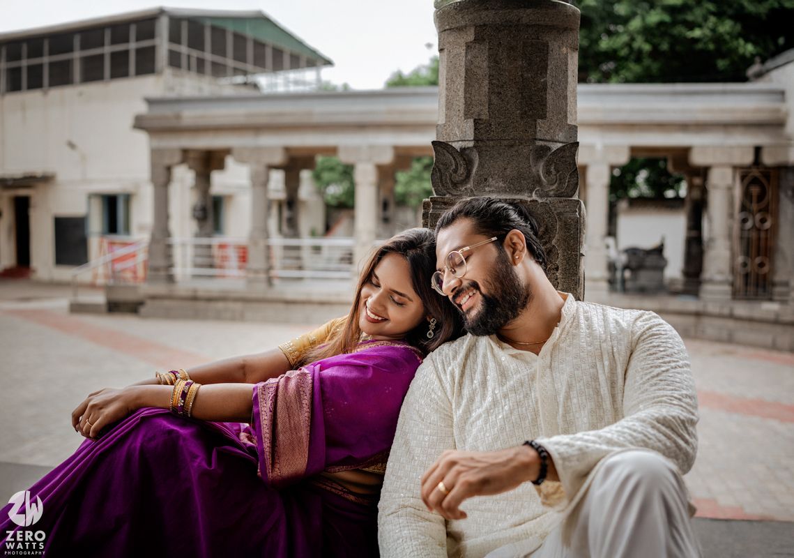 A couple in white and purple outfits sits together on stone steps in an outdoor setting.