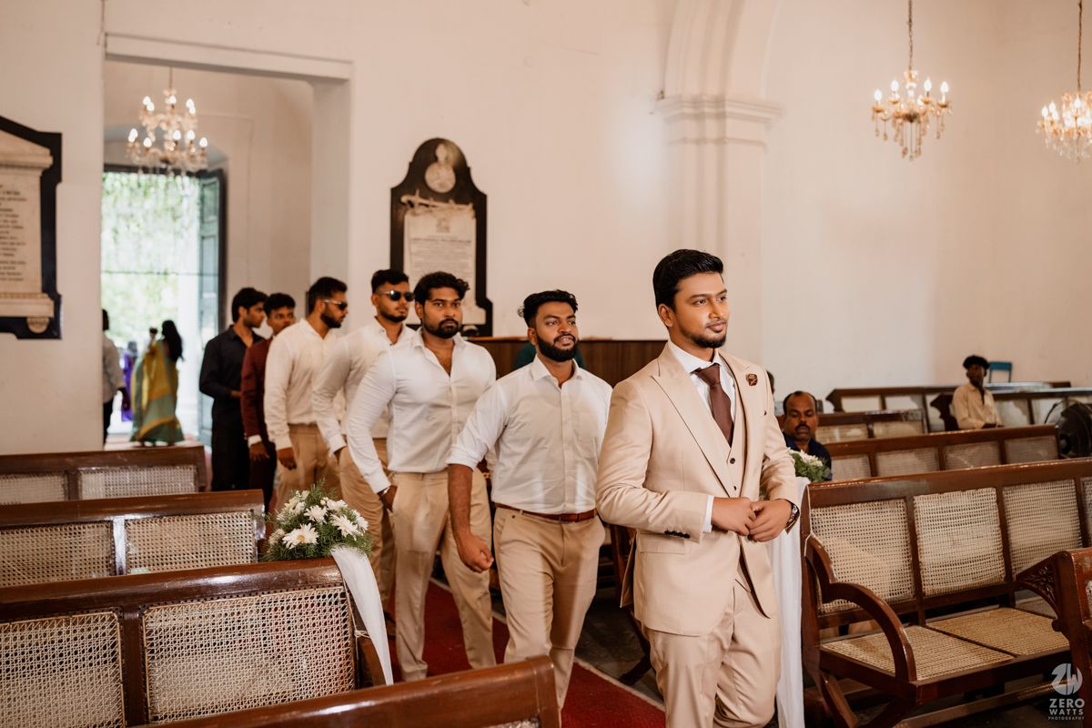 A wedding ceremony venue with white walls, crystal chandeliers, and wooden pews in classic church style.