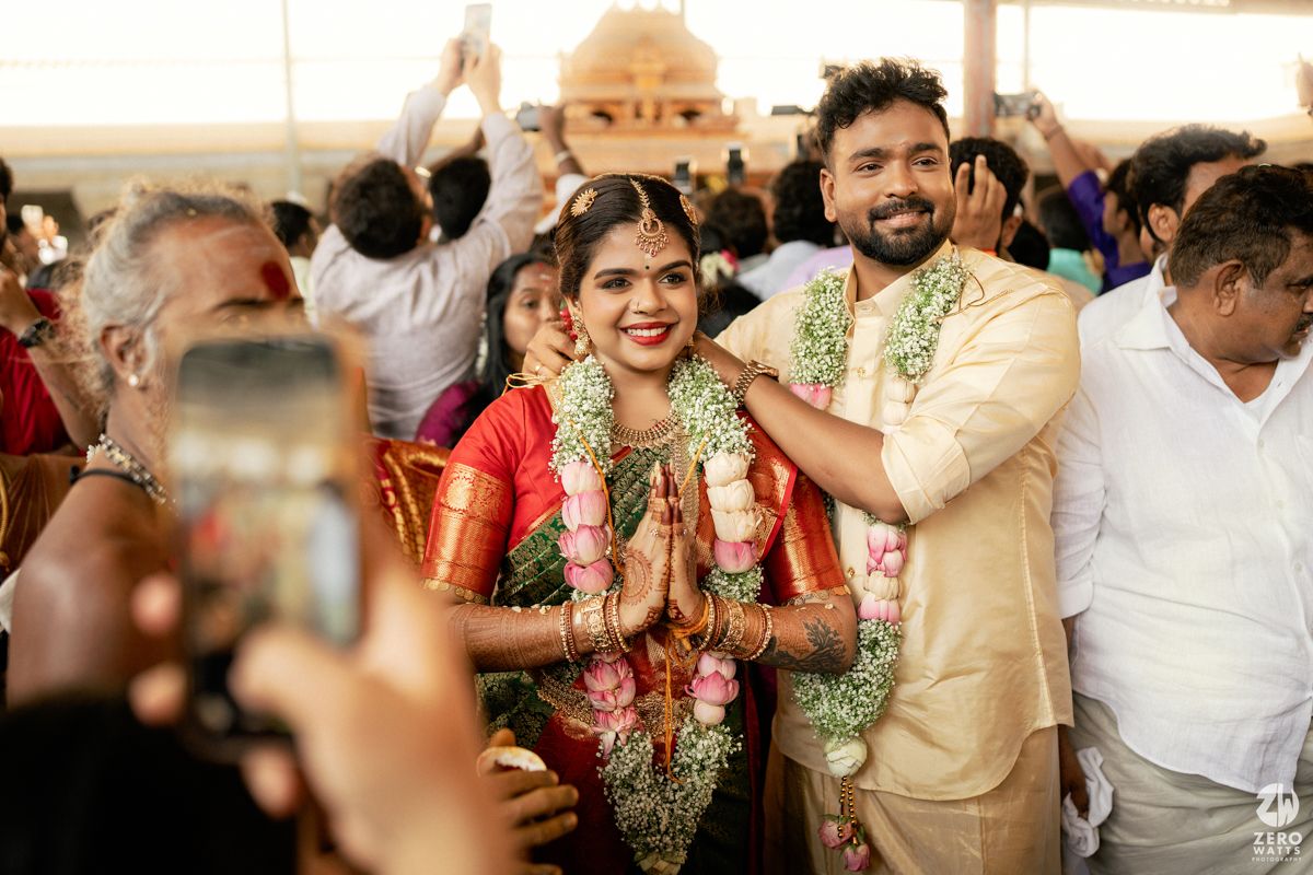 Indian bride and groom in traditional attire smiling at wedding ceremony with floral garlands.