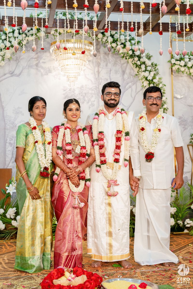 South Indian newlyweds posing with family in traditional wedding attire under floral decor.