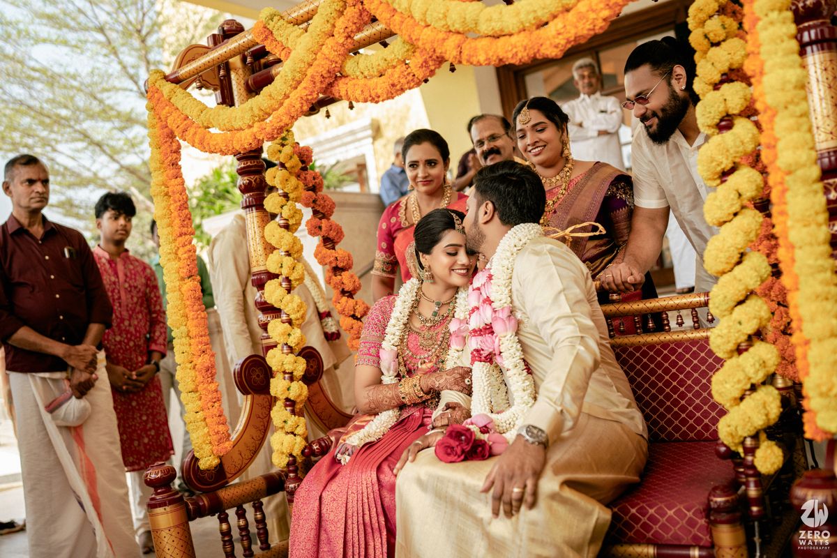 Indian wedding couple seated under floral mandap decorated with marigold garlands during traditional Hindu marriage ceremony.