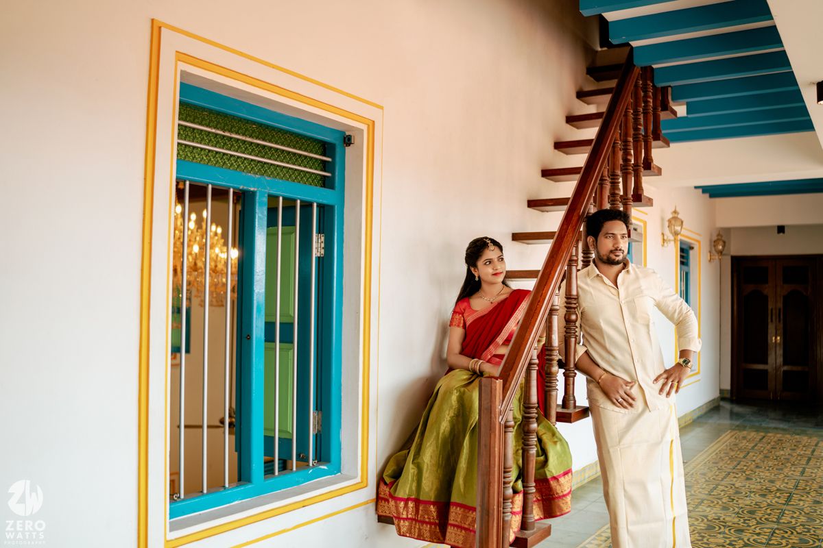 South Indian couple in traditional attire posing by colorful staircase in a heritage home.