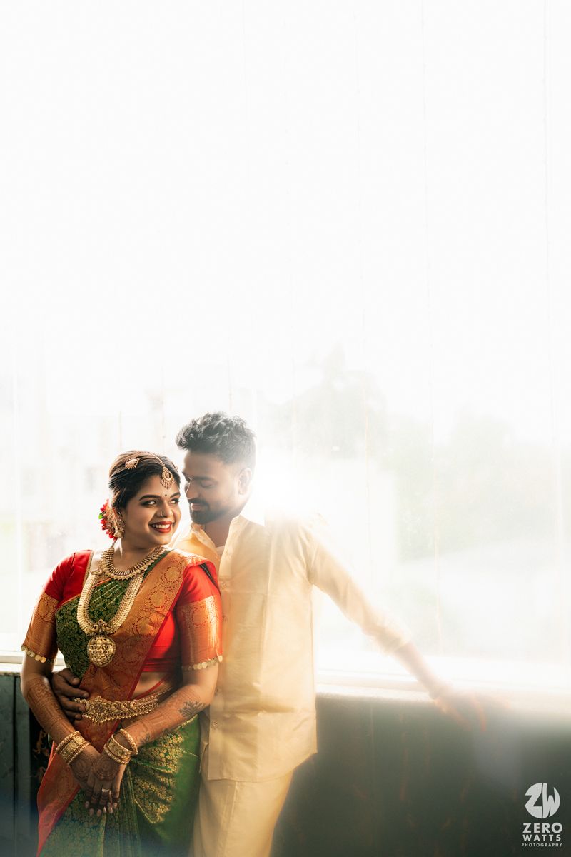 South Indian bride in green and red silk saree with gold jewelry poses with groom in white during wedding photoshoot.