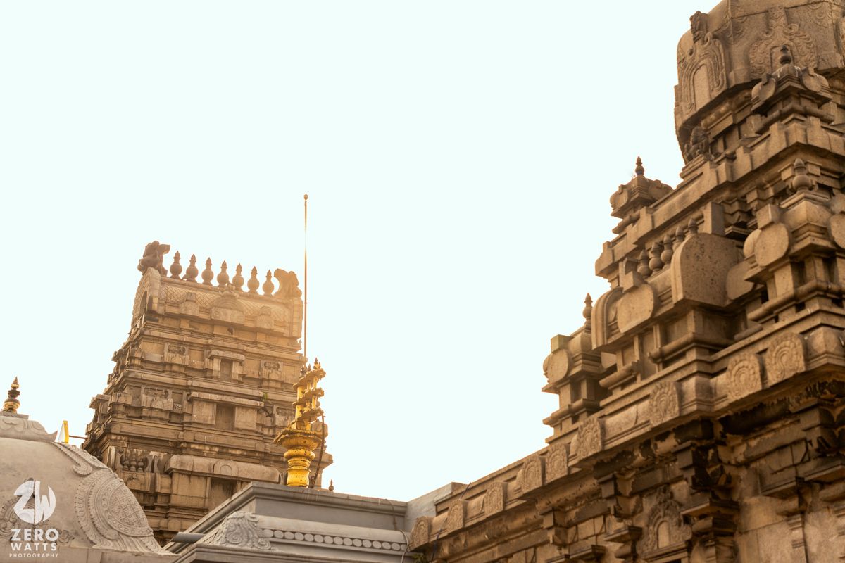 Ancient Hindu temple architecture with ornate stone carvings and golden gopuram tower against a bright sky.