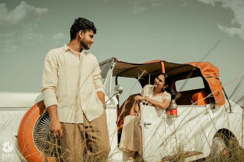 A romantic photoshoot in a grassy field with a vintage orange and white car during sunset.
