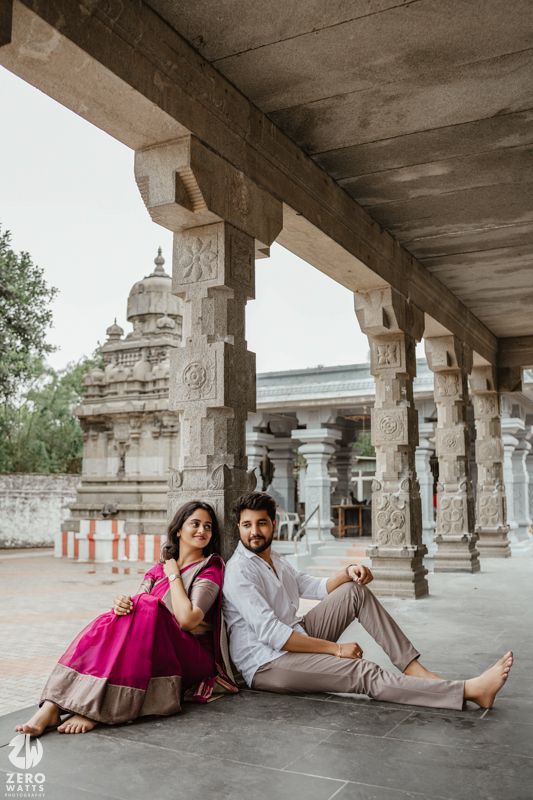 A couple relaxes in a traditional Indian temple corridor with stone pillars and carved details.