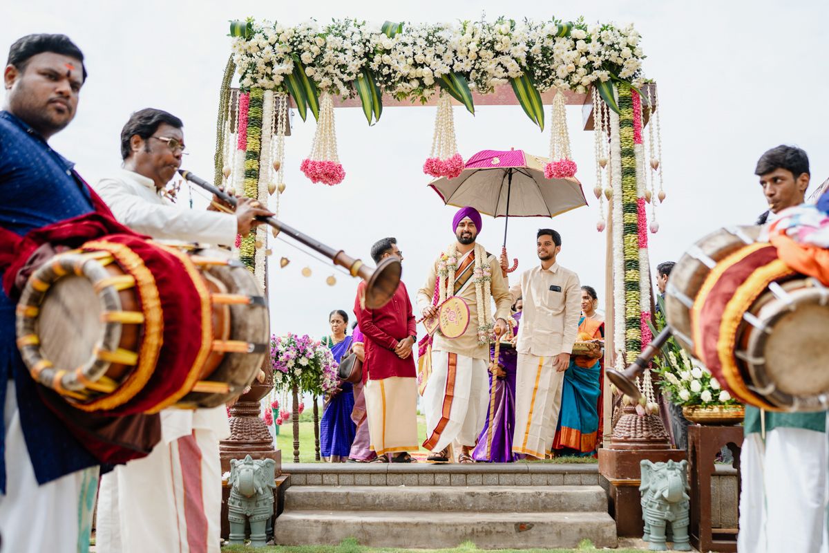 Outdoor wedding ceremony with white floral arch and traditional Indian decor elements.