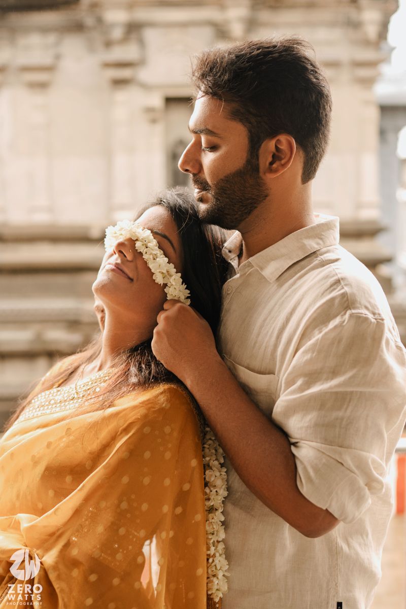 Romantic couple in traditional Indian attire share an intimate moment against stone architecture background.