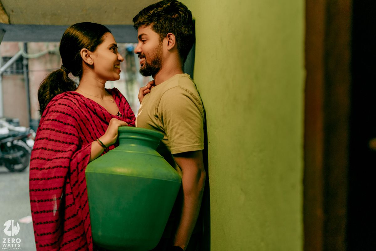 A couple in a romantic moment against a green wall with sunlight creating atmospheric shadows.