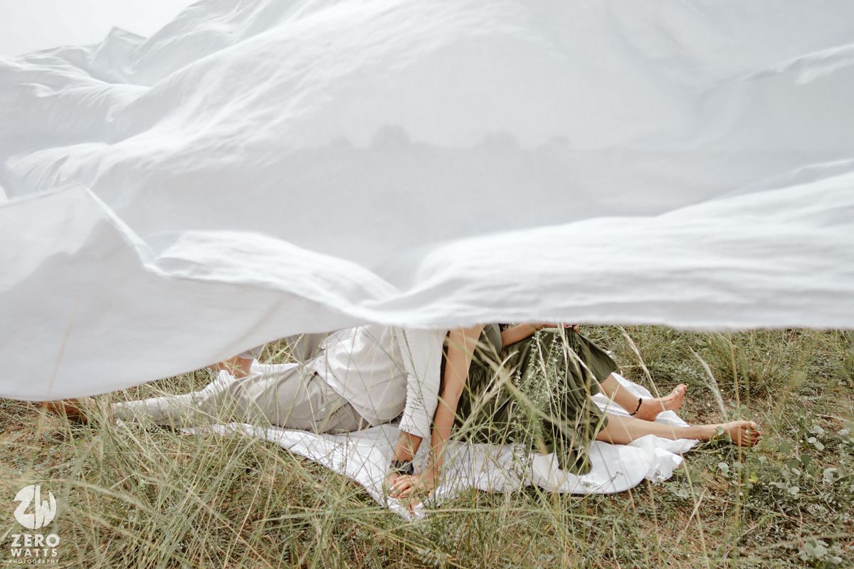 White fabric billowing in the wind across a grassy field on a cloudy day.