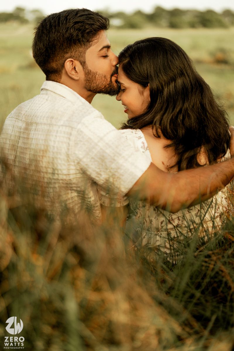 Intimate couple embracing in tall grass during golden hour sunset photoshoot.