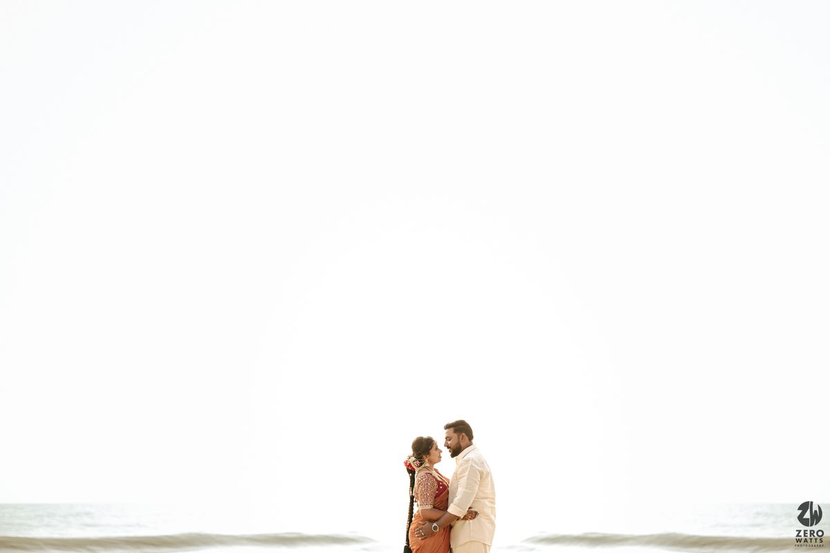 Two people walking along a serene beach at sunset with a gentle ocean surf in the background.