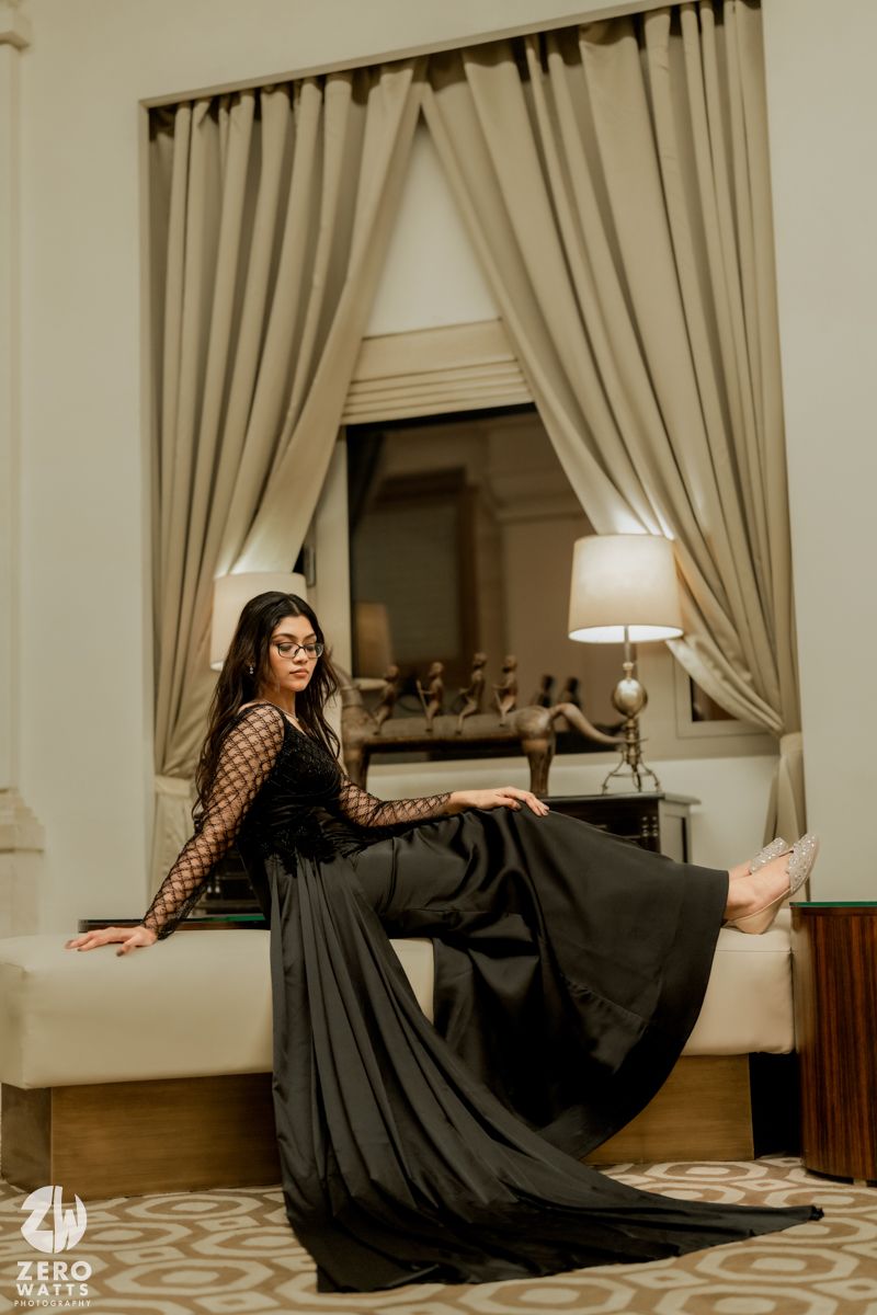 A flowing black dress twirls gracefully across a room with beige curtains and patterned carpet.