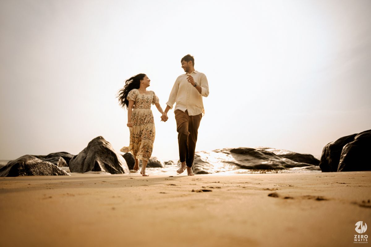 Two silhouetted figures walk hand in hand along a misty beach at sunset creating a romantic atmosphere.