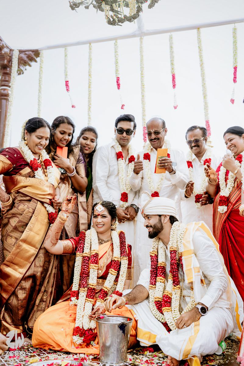 Indian bride and groom in traditional attire with floral garlands during a South Indian wedding ceremony surrounded by family.