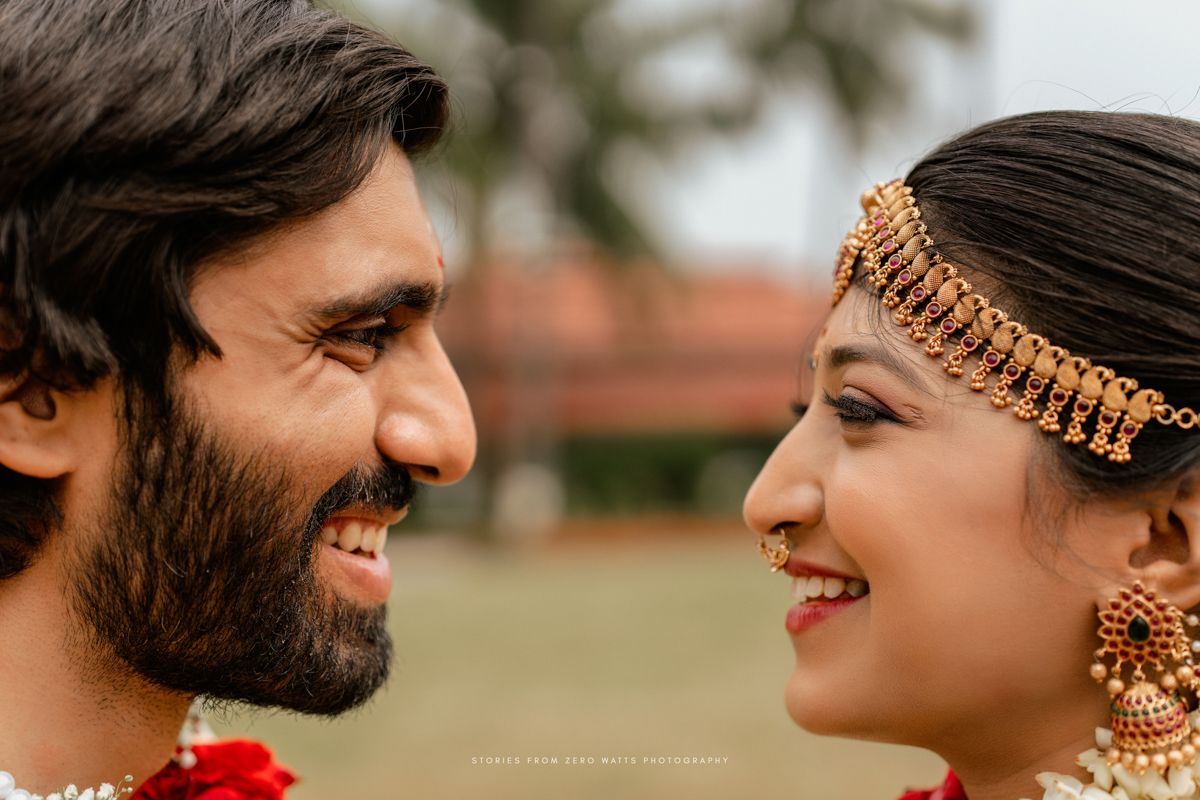 South Indian couple in traditional wedding attire share a joyful moment, bride adorned with gold jewelry and maang tikka.