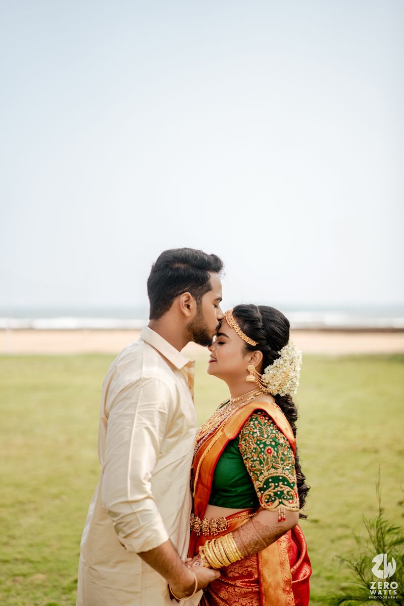 South Indian bride and groom in traditional wedding attire share a romantic moment near a beach.
