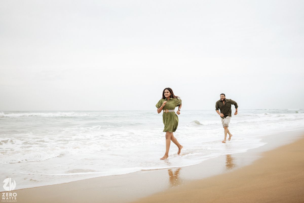 People walking along a misty beach shoreline during an overcast day as waves crash on the sand.