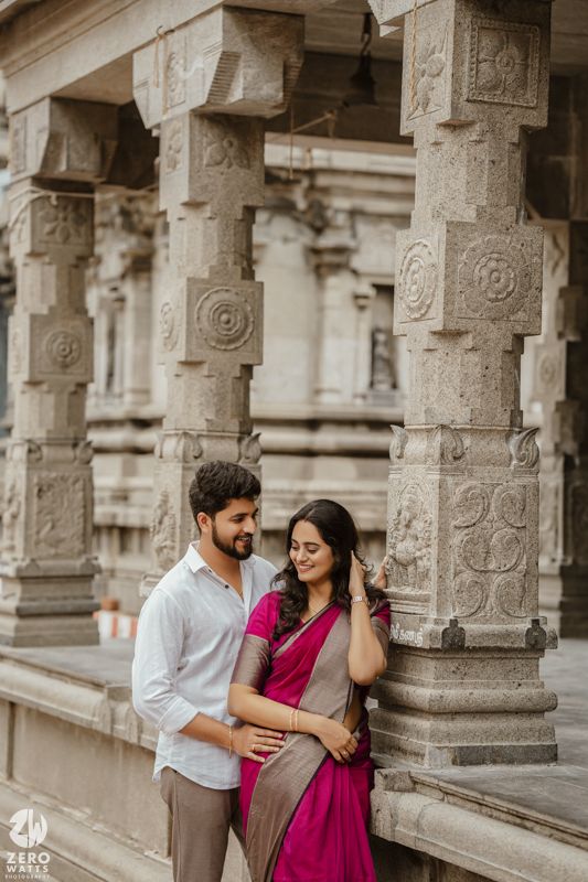 A couple shares romantic moments among ornate stone pillars in traditional Indian attire.