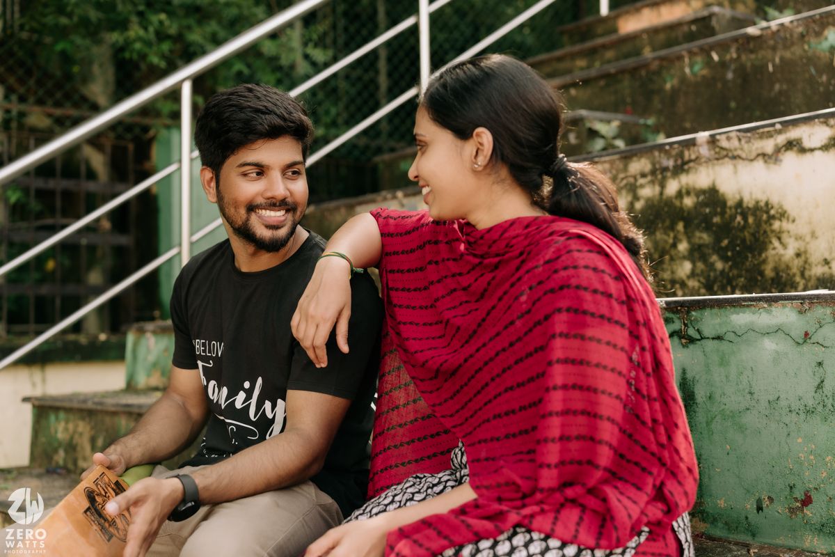 A couple in casual attire sits together and shares food while enjoying an outdoor meal on concrete steps.