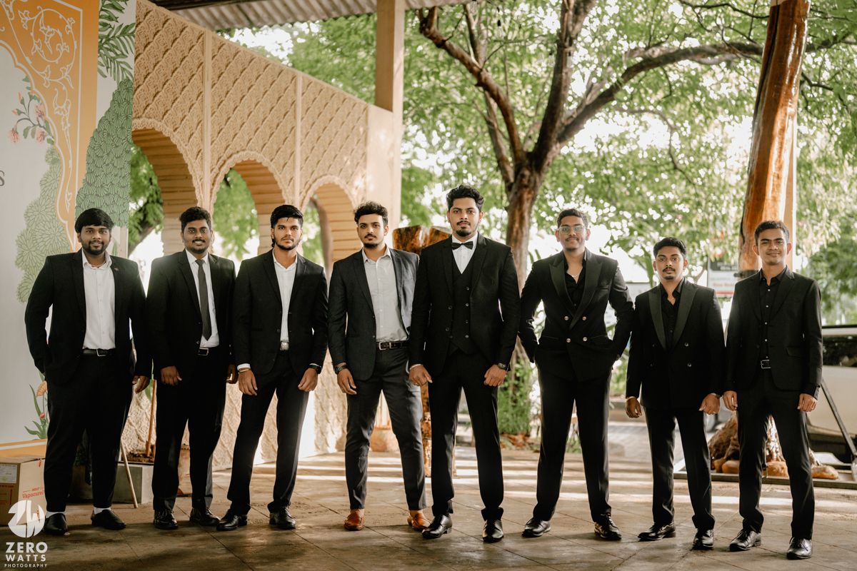 A row of groomsmen in black suits and ties show off their colorful socks while posing together outdoors.