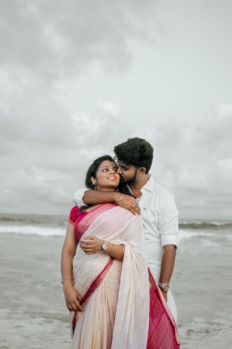 A romantic moment captured on a cloudy beach with waves crashing in the background.