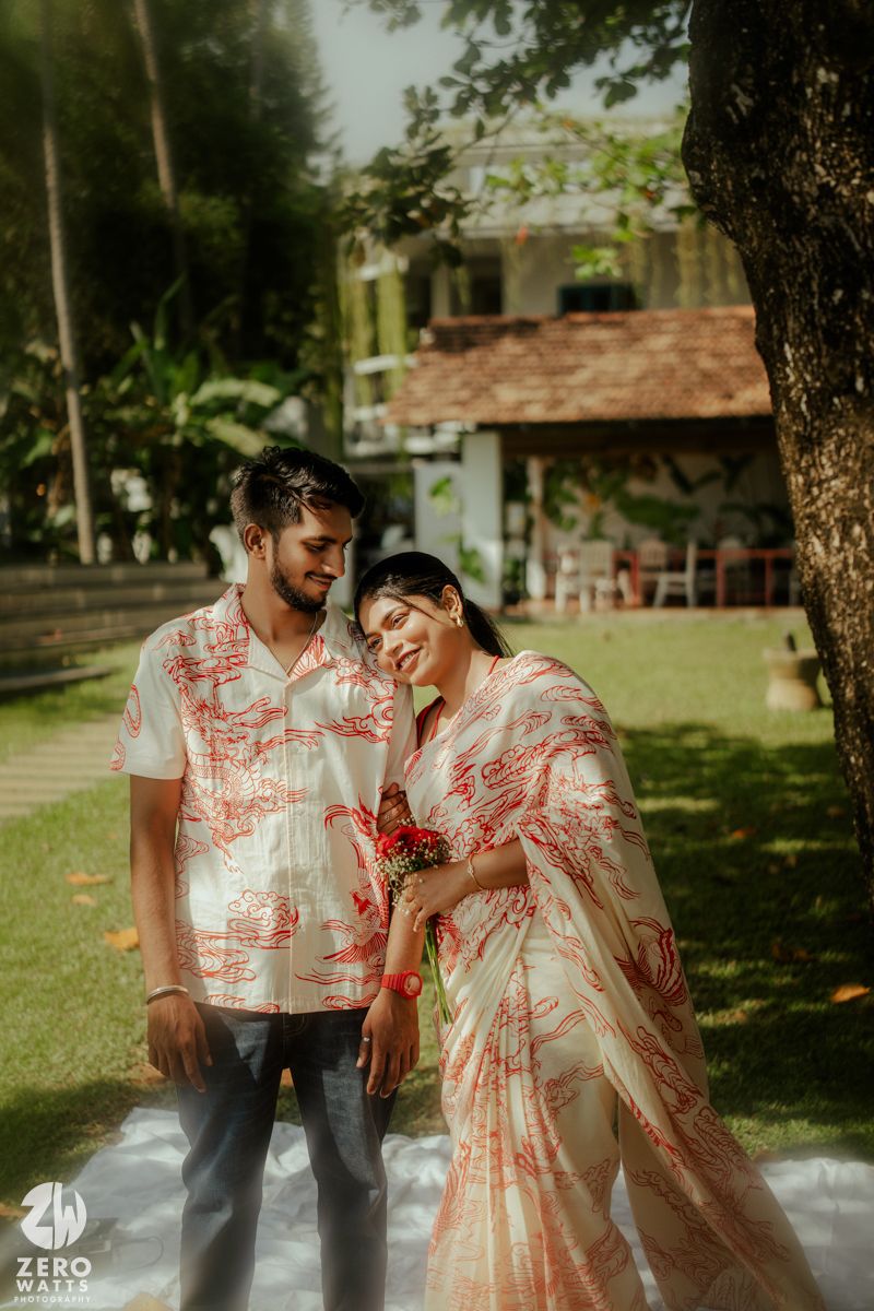 Couple in coordinated red and white outfits poses together in a garden setting for romantic photoshoot.