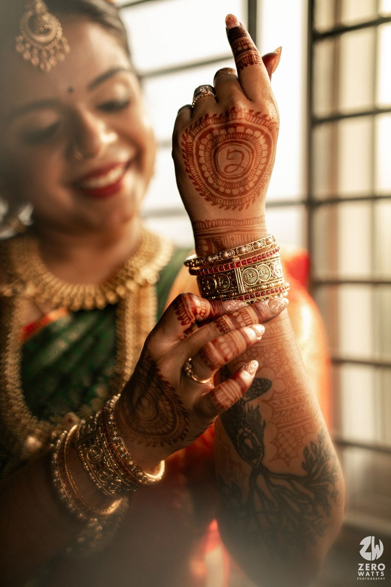Indian bride showcasing intricate mehndi henna designs on hands with gold bangles and traditional bridal jewelry.