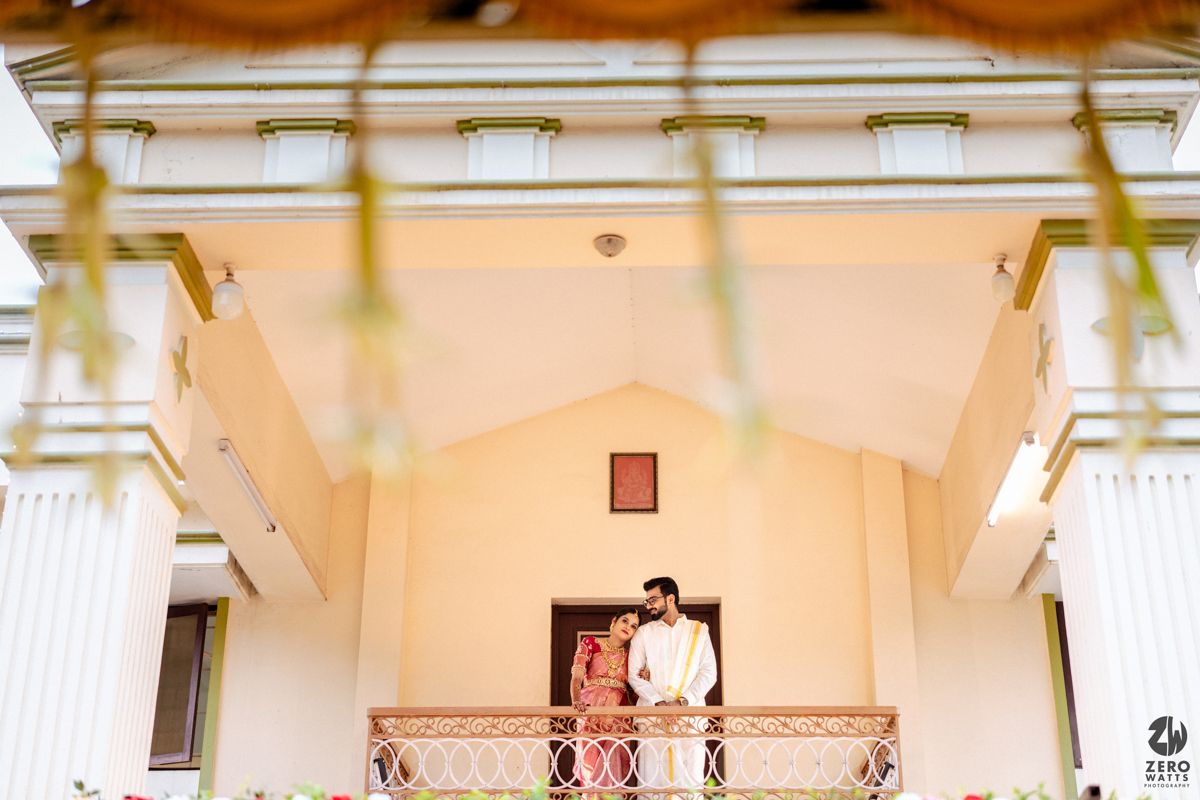 Indian wedding couple standing on balcony of decorated venue during traditional South Indian wedding ceremony.
