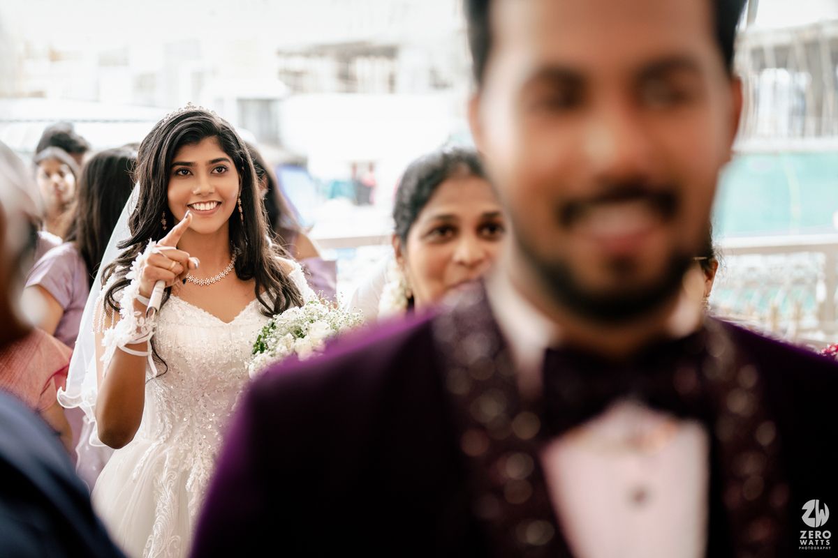 Smiling bride in white gown walks toward groom in purple tuxedo during Christian wedding ceremony.