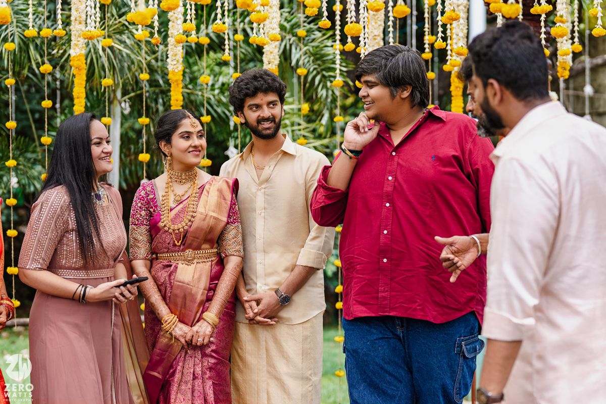 Wedding celebration with guests in traditional attire mingling under yellow floral decorations.