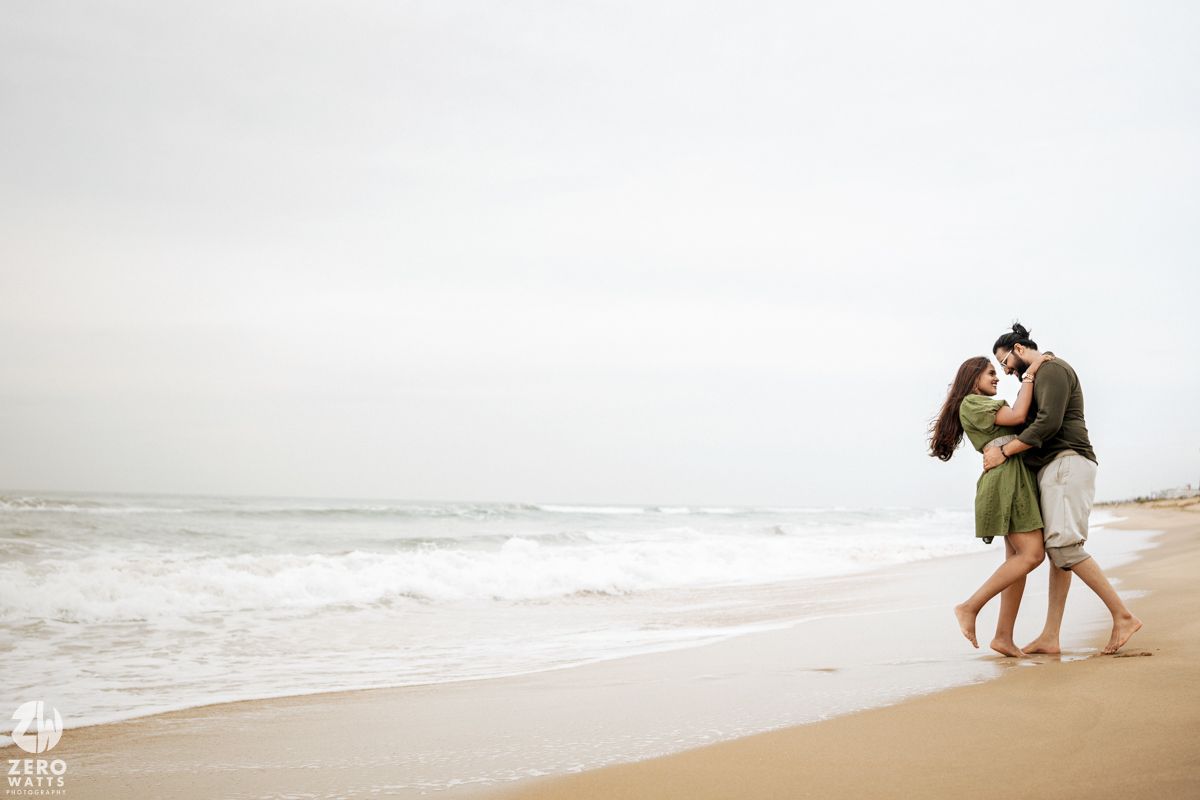 Two people share a playful moment together while walking on a sandy beach near the ocean waves.