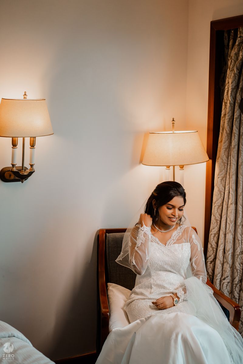 A person in a white wedding dress sits quietly in a room illuminated by warm lamplight.