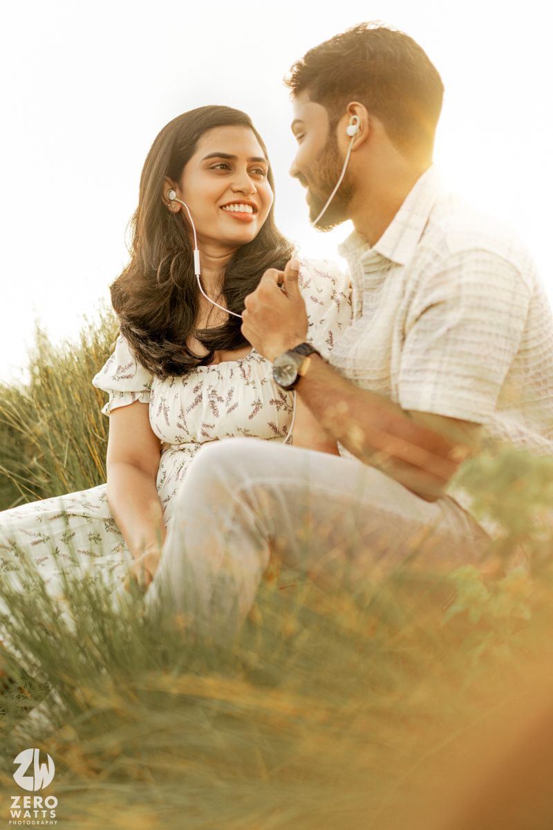 A couple sits together in tall grass during golden hour with soft sunlight filtering through.