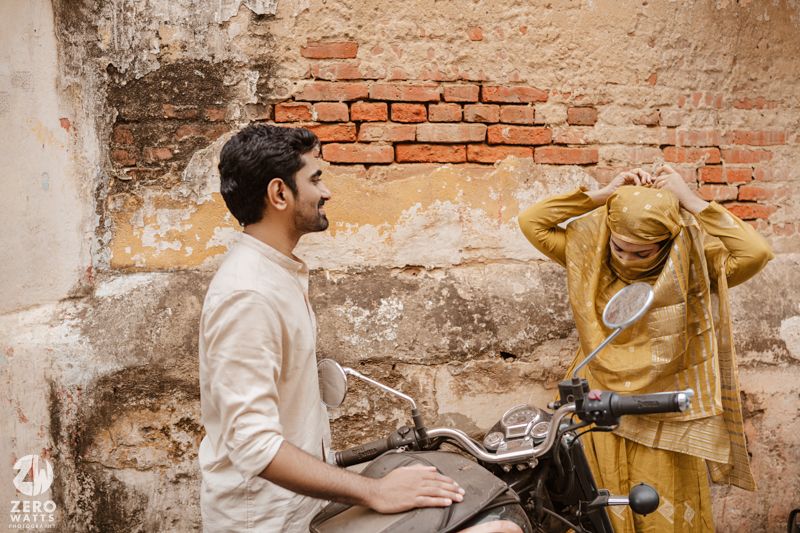 Two people in casual clothing dancing together beside a weathered brick wall.