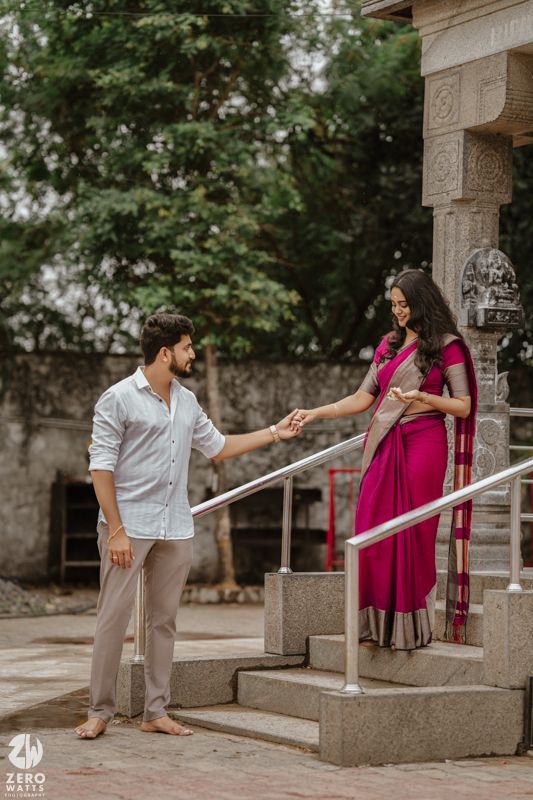 Couple holds hands playfully on temple steps surrounded by carved stone pillars and greenery.